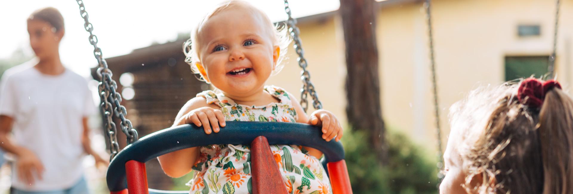 Lächelndes Baby auf einer Schaukel im sonnigen Park.