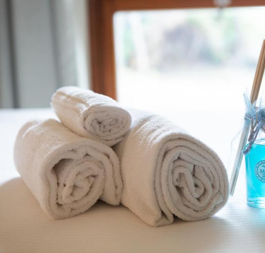 Rolled white towels next to a blue fragrance diffuser on a bed.