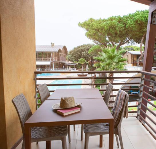 Balkon mit Tisch, Stühlen, Poolblick und Garten.