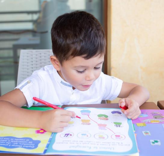 Bambino disegna con un pennarello rosso su un libro colorato.