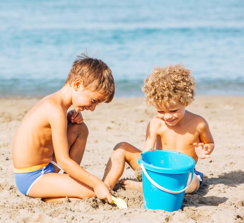 Due bambini giocano sulla spiaggia con un secchiello.